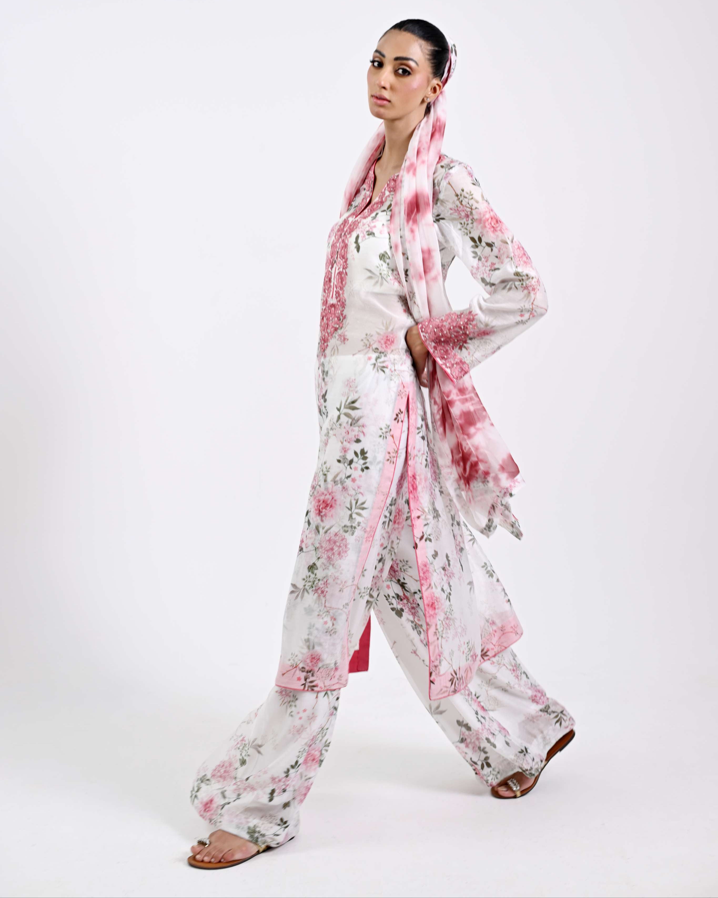 Woman wearing a floral outfit with a pink scarf on a white background