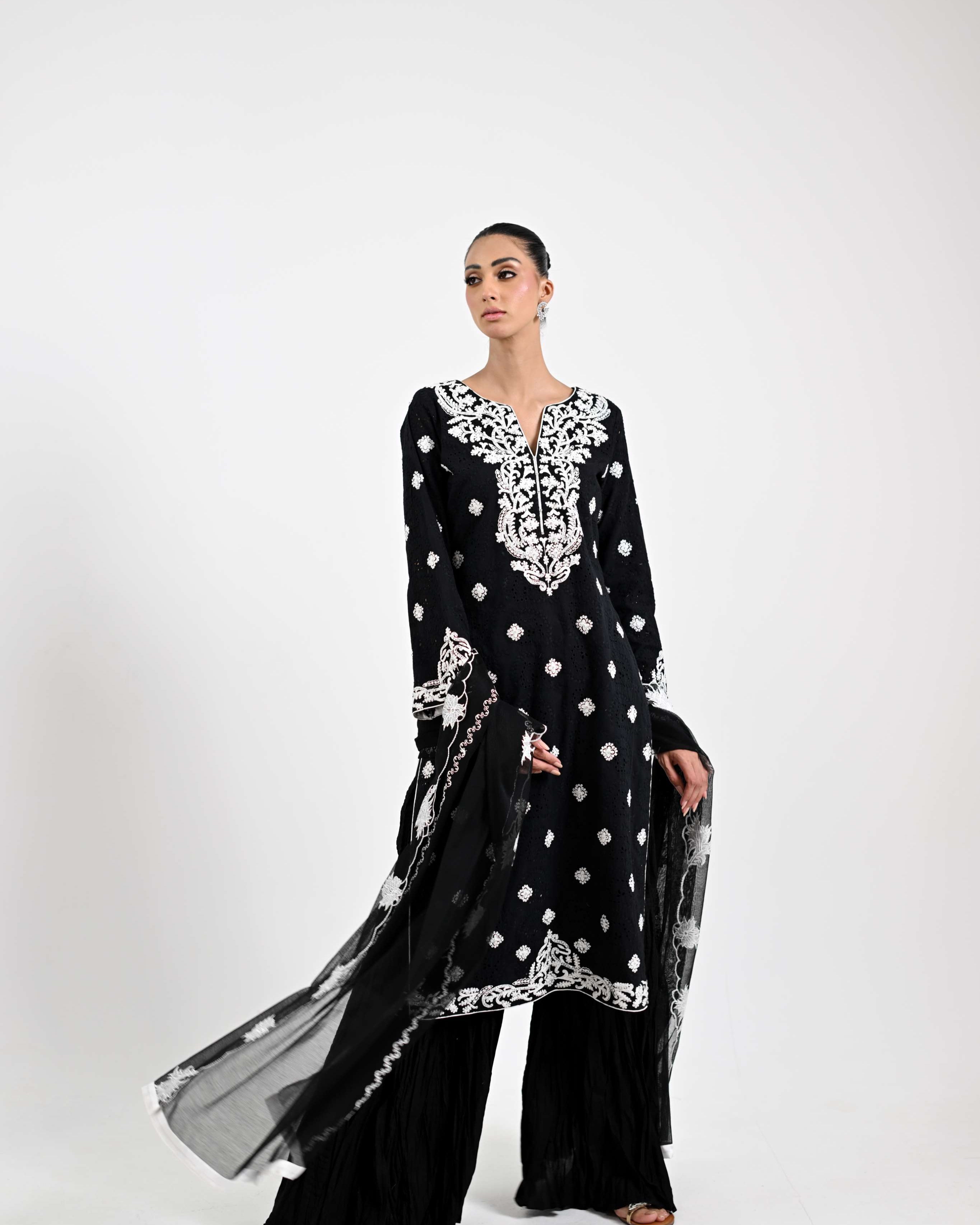 Woman wearing a black and white embroidered outfit on a white background