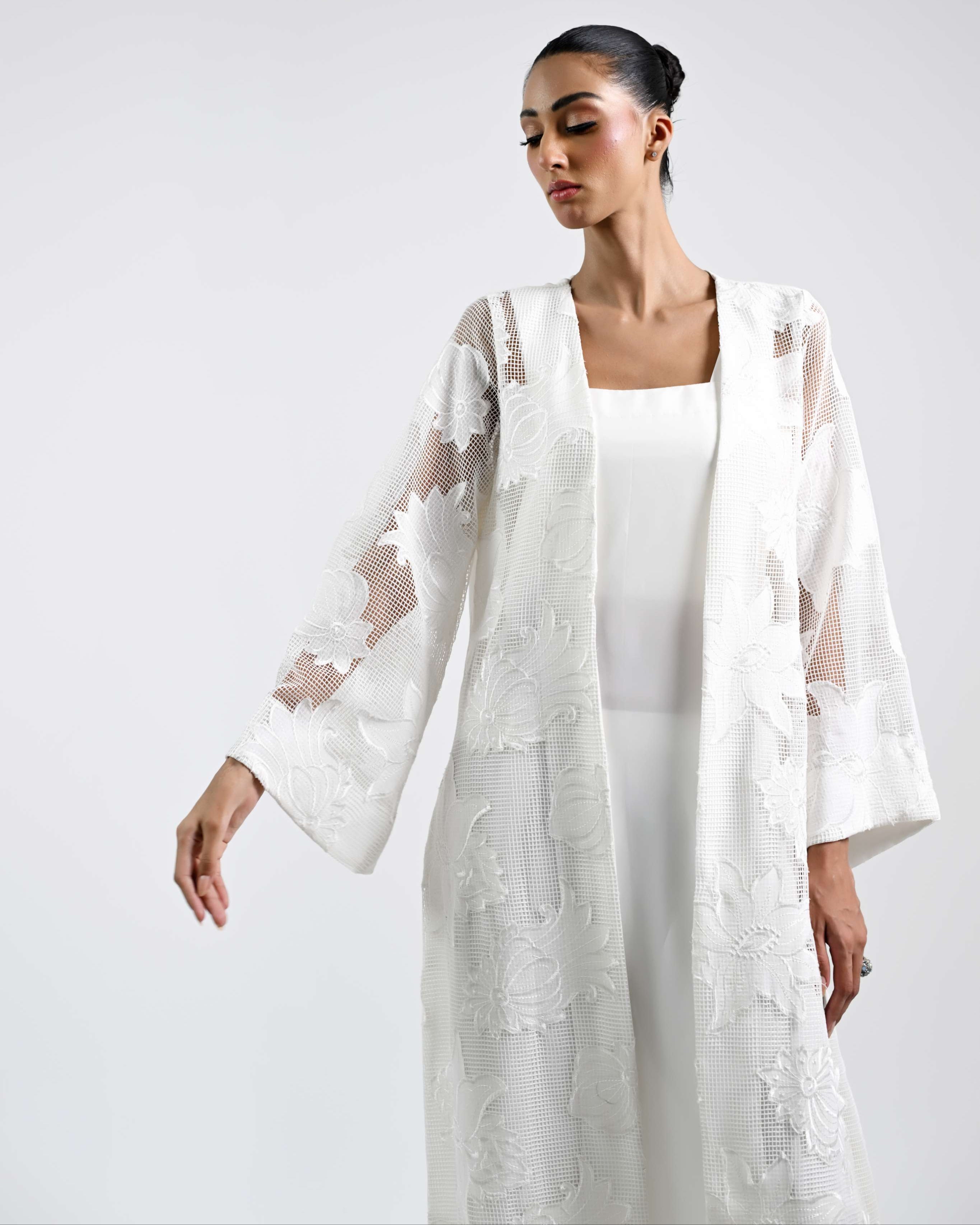Woman wearing a white outfit with floral lace details on a plain background