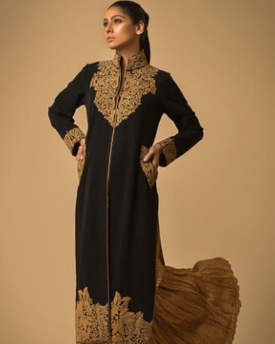 Black and gold traditional outfit with intricate embroidery on a beige background
