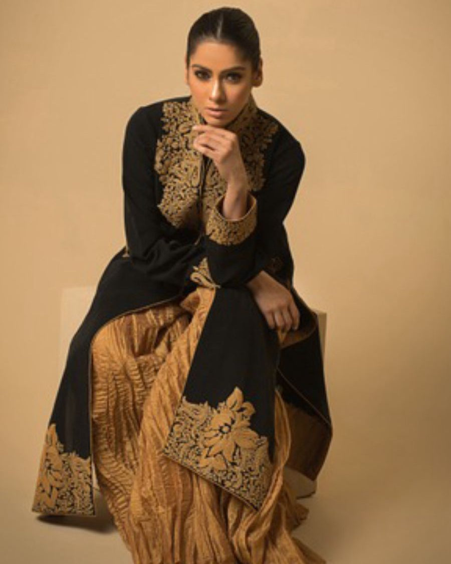 Woman wearing a black and gold traditional outfit against a beige background
