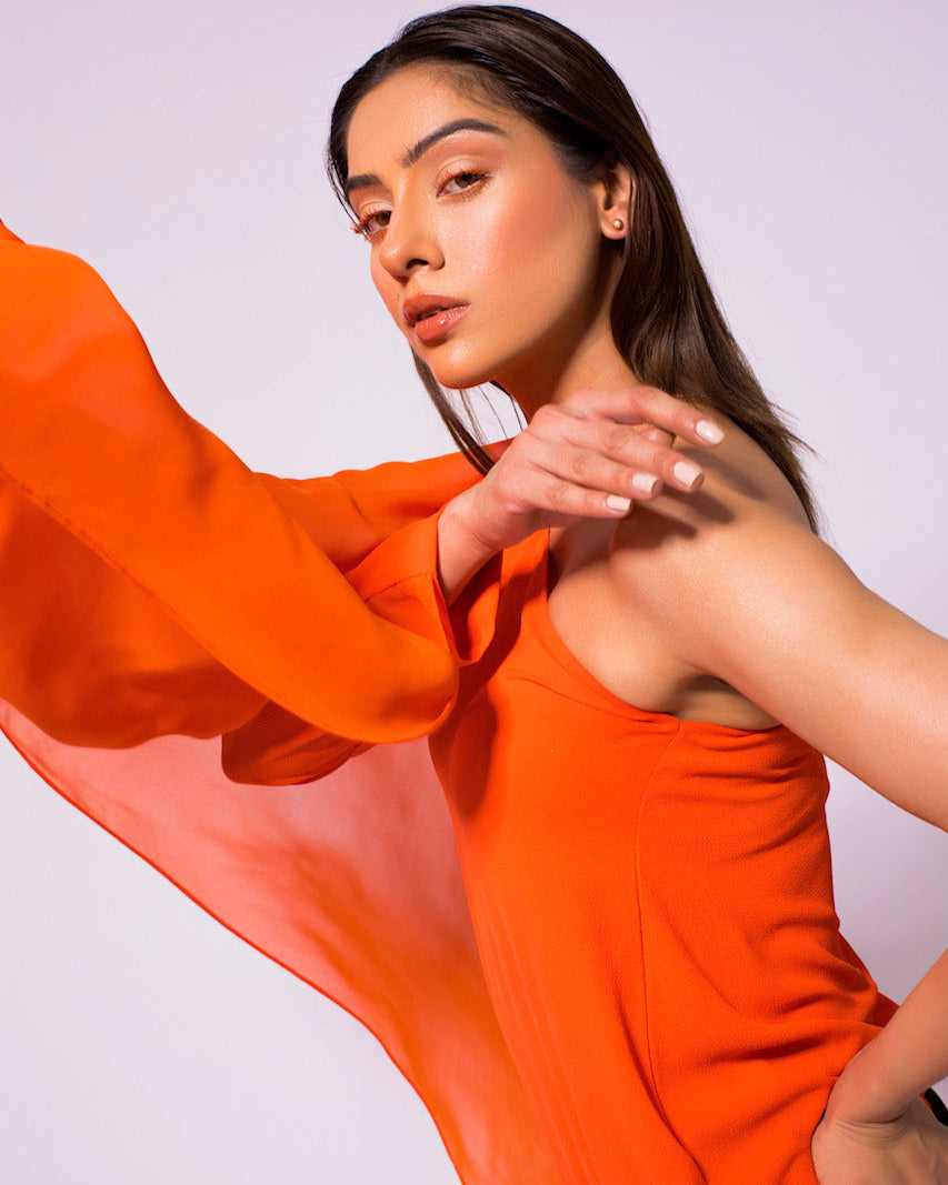 Woman wearing an orange dress with a flowing fabric against a plain background