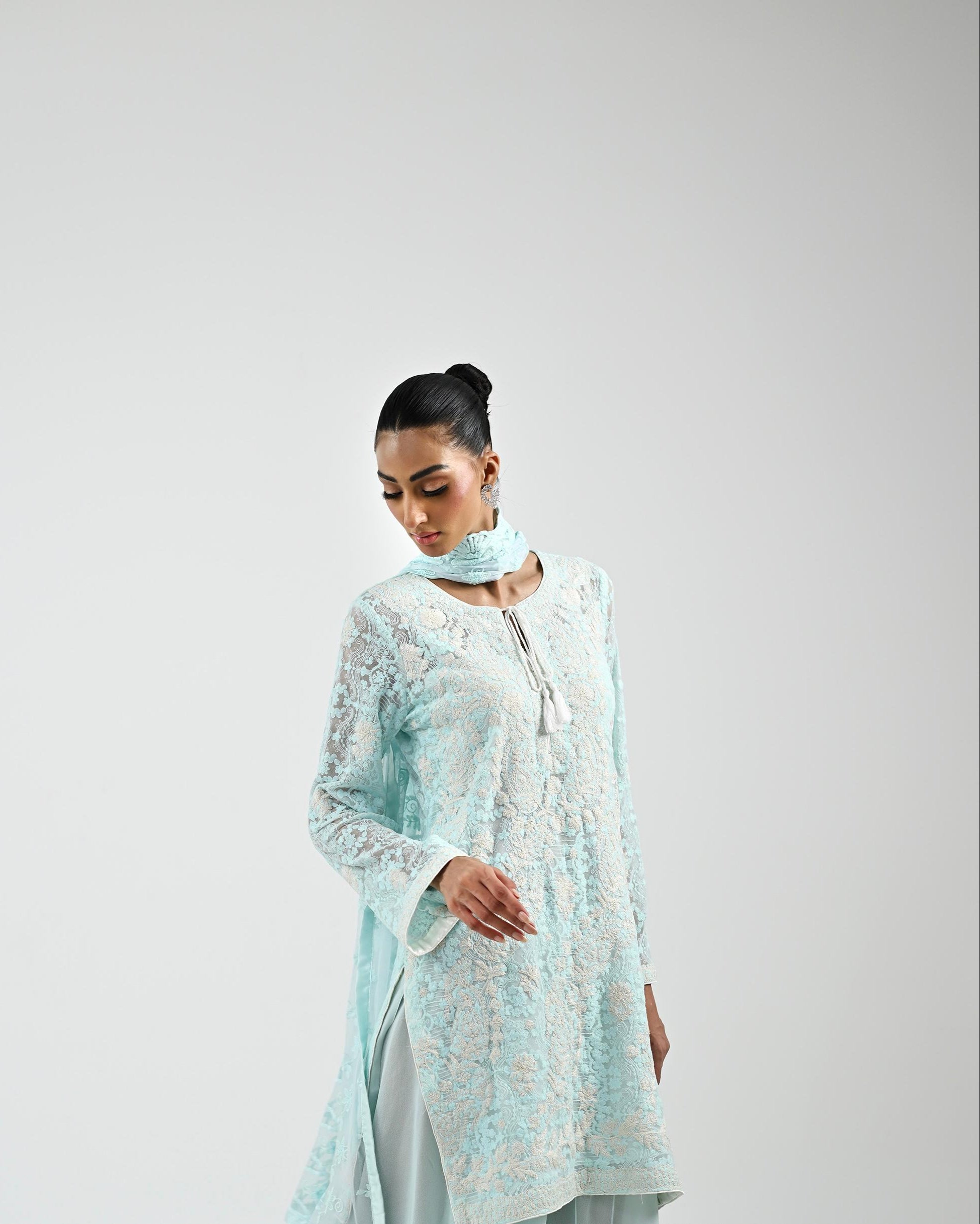 Woman wearing a light blue embroidered outfit on a plain background