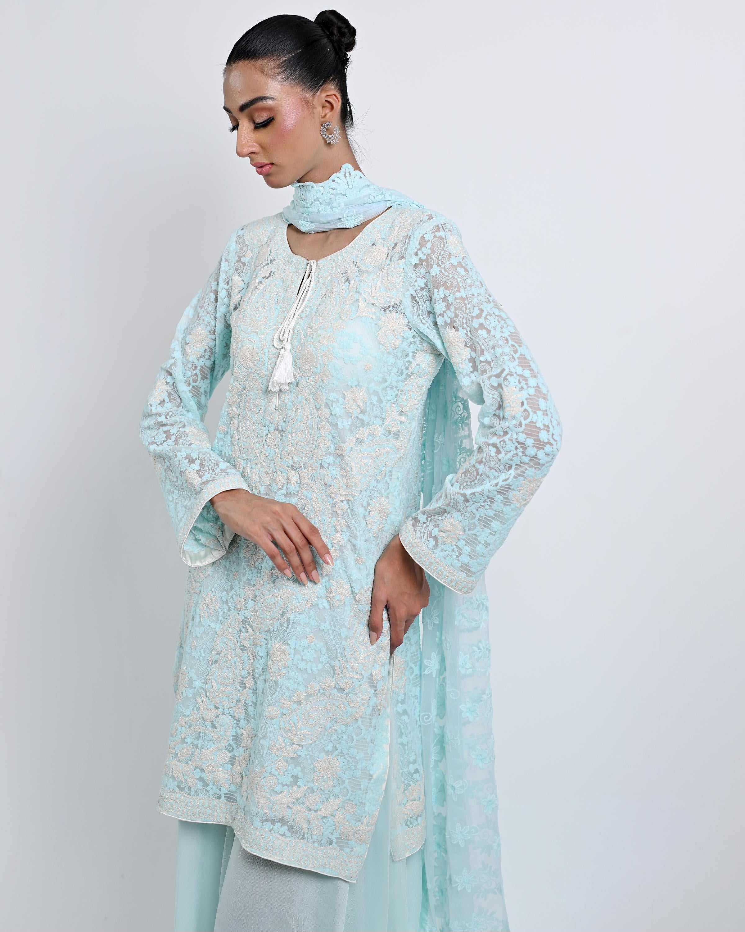 Woman wearing a light blue embroidered outfit against a white background