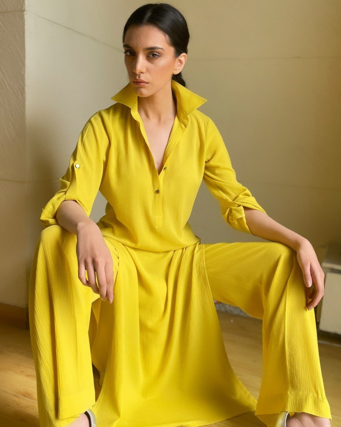 Woman wearing a yellow outfit sitting on a wooden floor.