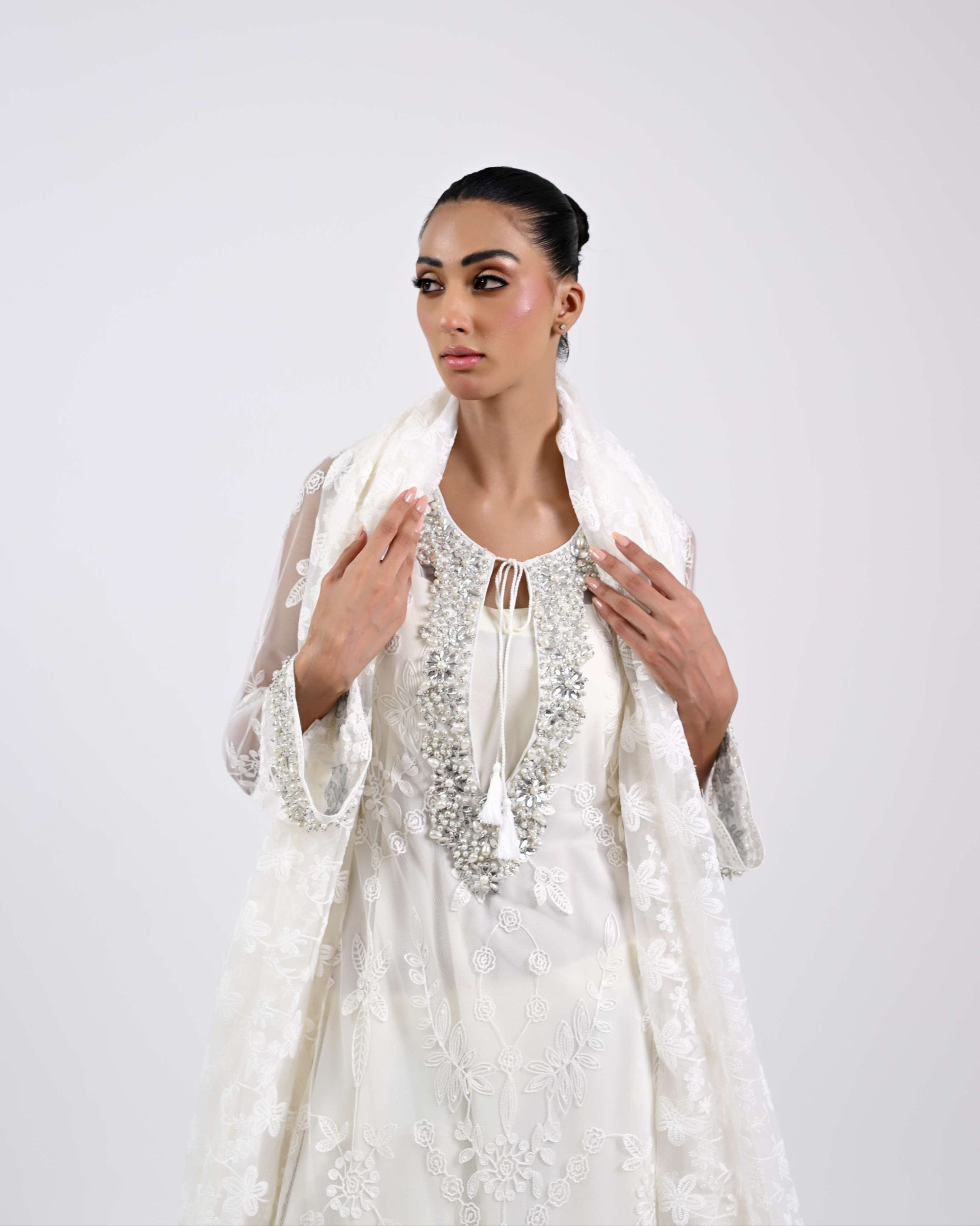 Woman wearing a white embroidered outfit on a plain background