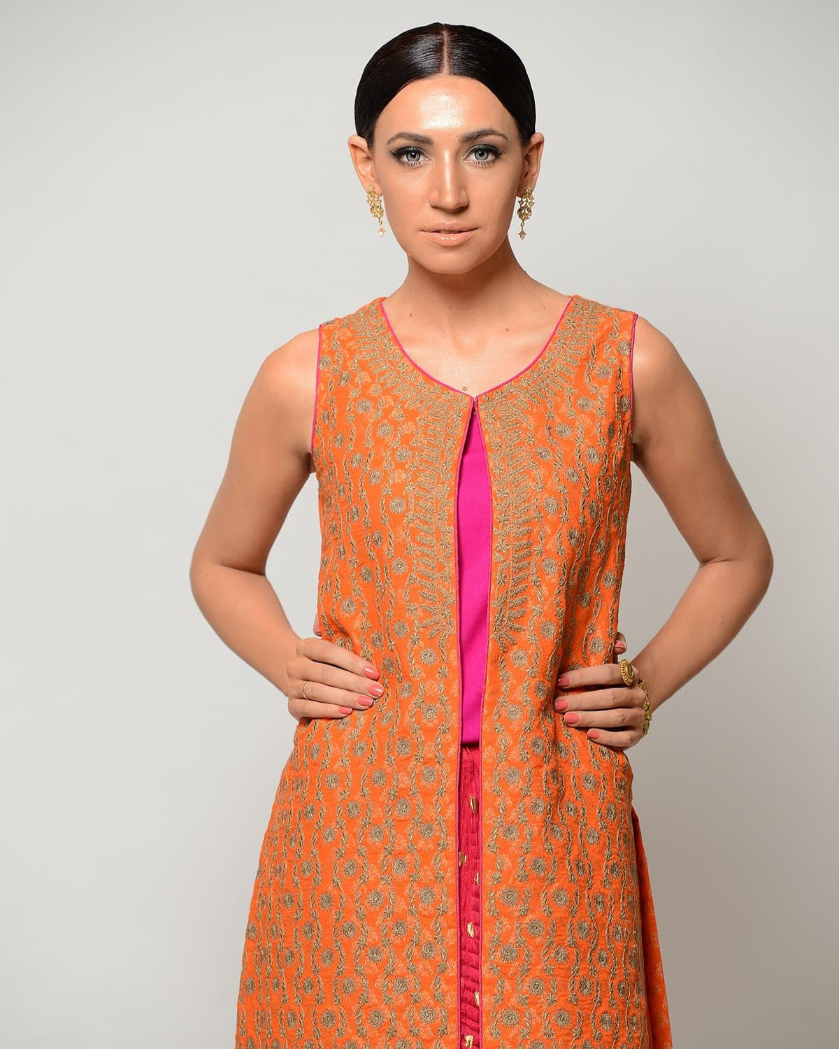 Woman wearing an orange and pink traditional outfit against a plain background