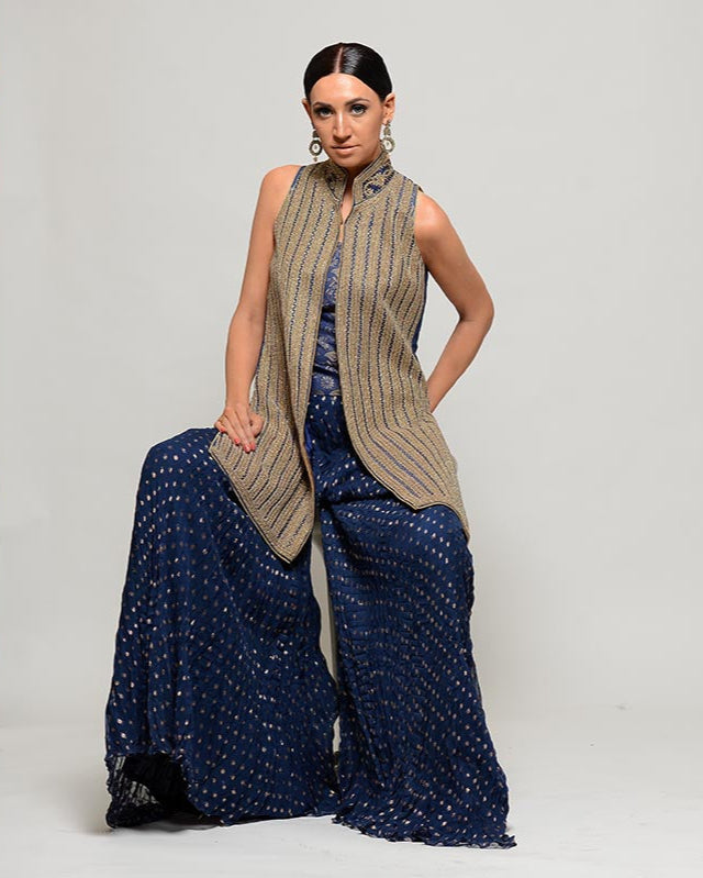 Woman wearing a beige vest and blue patterned pants in a studio setting