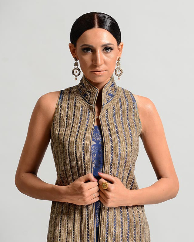 Woman wearing a patterned vest over a dress on a plain background