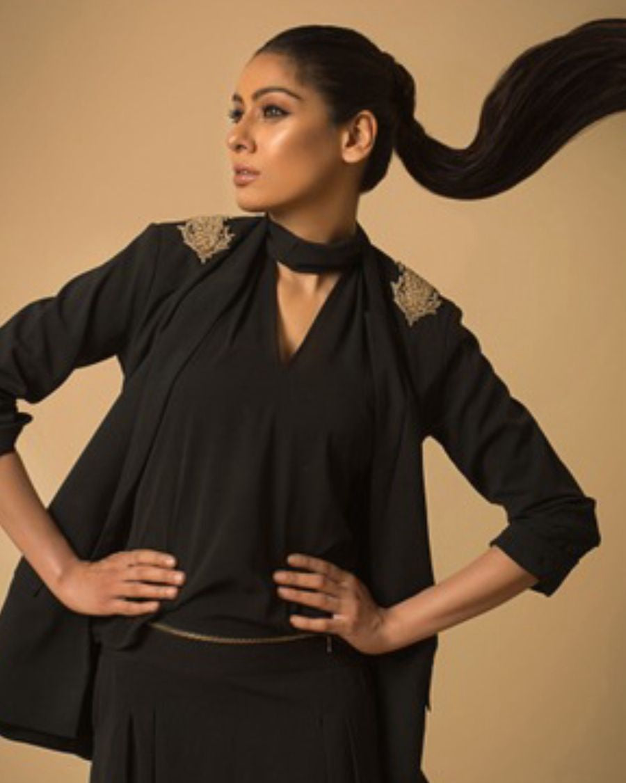 Woman wearing a black outfit with gold accents against a beige background