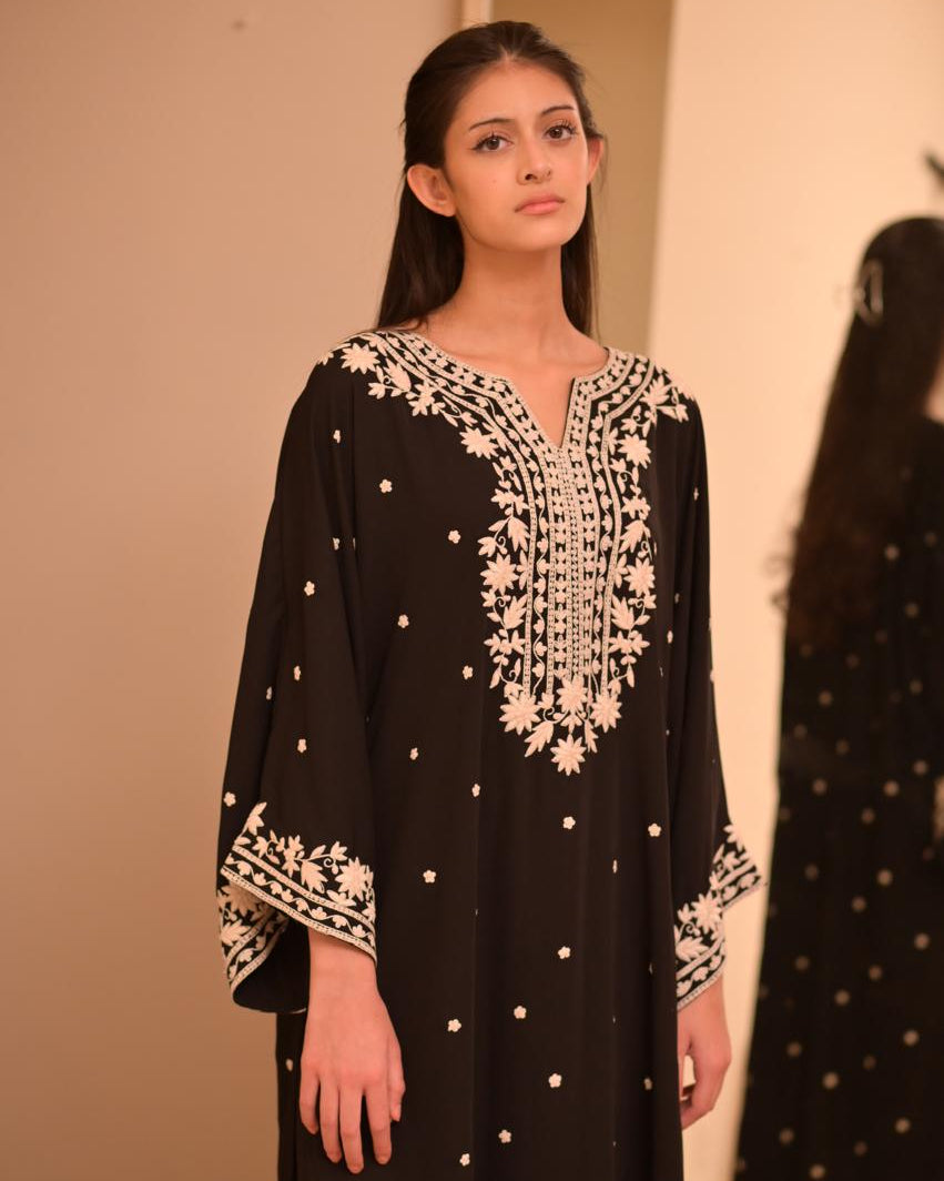 Black garment with white floral embroidery on a plain background