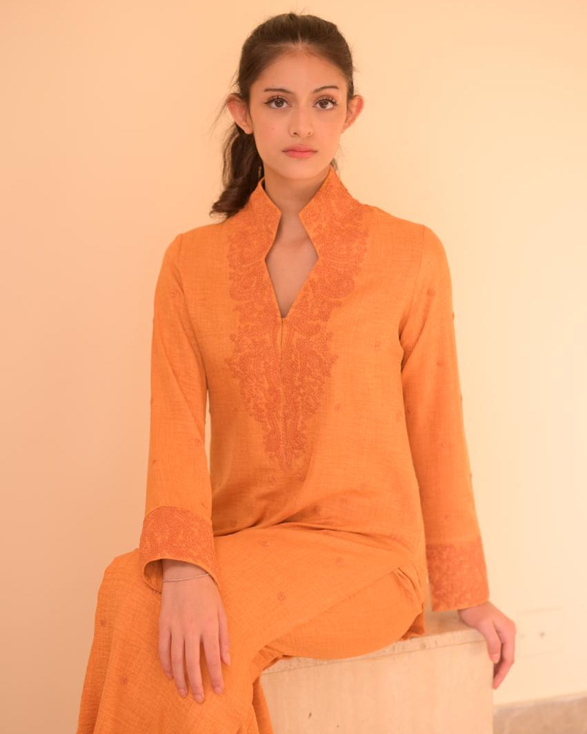 Woman in an orange traditional outfit standing in a room with a mirror.