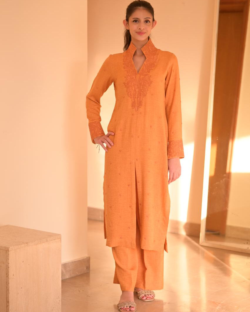Woman wearing an orange traditional outfit in a softly lit room.