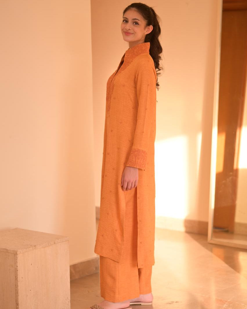 Woman in an orange traditional outfit standing in a room with a mirror.