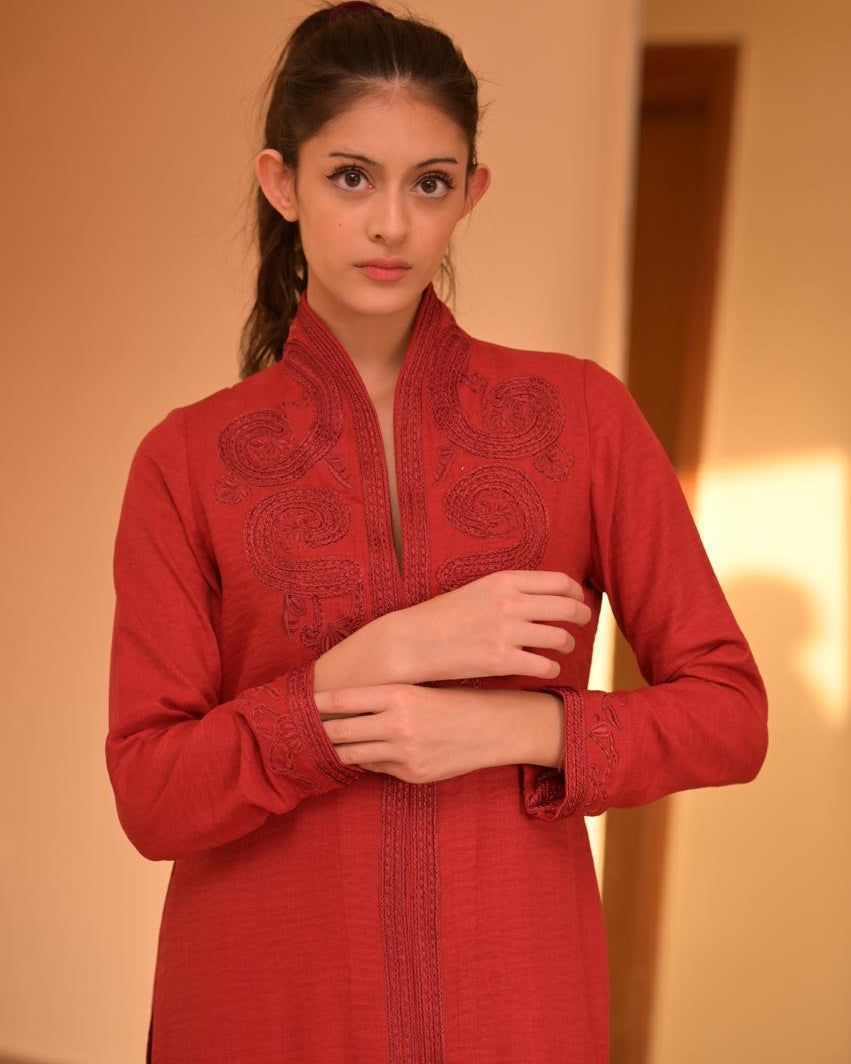 Woman wearing a red embroidered traditional outfit against a neutral background